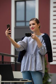 Charming happy woman student communicates by phone and use laptop computer to prepare for the course work. Concept of working outdoors