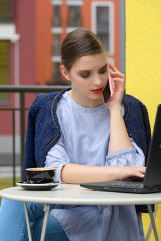 Charming happy woman student communicates by phone and use laptop computer to prepare for the course work. Concept of working outdoors