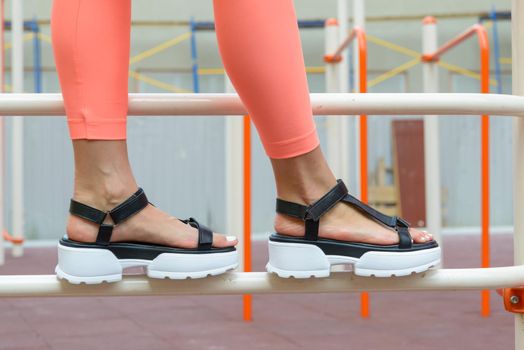 Sexy woman's sunburnt legs wearing black sandals and peach leggings, outdoors. white pedicure