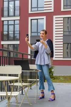 Charming happy woman student communicates by phone and use laptop computer to prepare for the course work. Concept of working outdoors