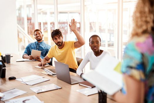 Cropped shot of a handsome young male designer raising his hand while sitting in the boardroom during a meeting.