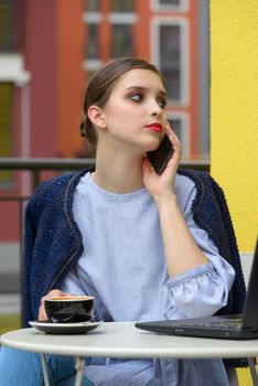 Charming happy woman student communicates by phone and use laptop computer to prepare for the course work. Concept of working outdoors