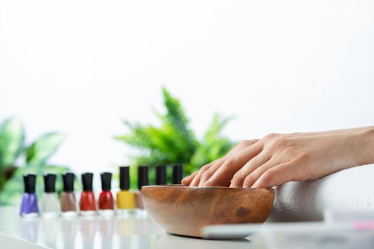 Woman hands in wooden bowl with water. Spa procedure and relaxation. Female hands preparing for manicure. Professional nail care and beautician service. Beauty and healthy lifestyle.