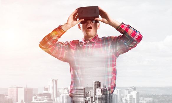 Young man with virtual reality headset or 3d glasses over cityscape background