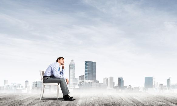 young businessman sits on an office chair, thoughtful and looking up