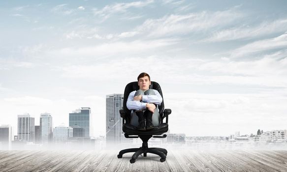 scared businessman sitting on a chair with his hands clasped his knees