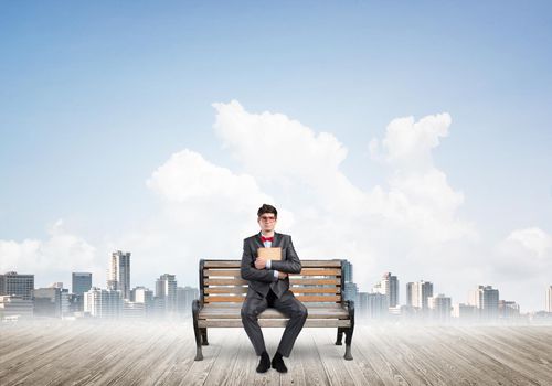 Student sits on a bench, holding a book. Traditional education concept