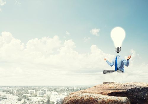 Businessman sitting in lotus pose and light bulb instead of his head