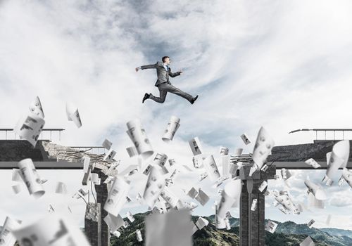 Businessman jumping over gap in bridge among flying papers as symbol of overcoming challenges. Skyscape and nature view on background. 3D rendering.