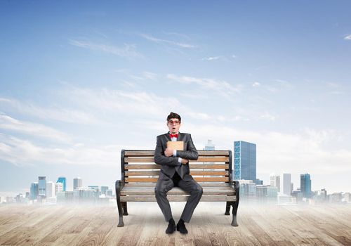 Student sits on a bench, holding a book. Traditional education concept