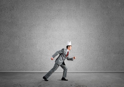 Young handsome businessman wearing white paper crown running in a hurry