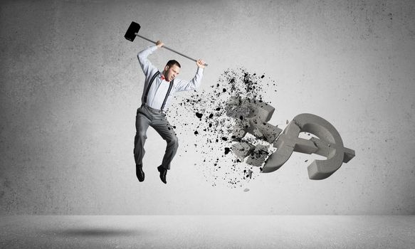 Young furious businessman crashing with hammer stone dollar symbol