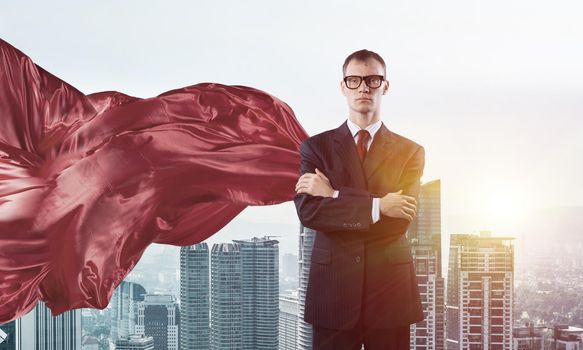 Young confident businessman wearing red cape against modern city background