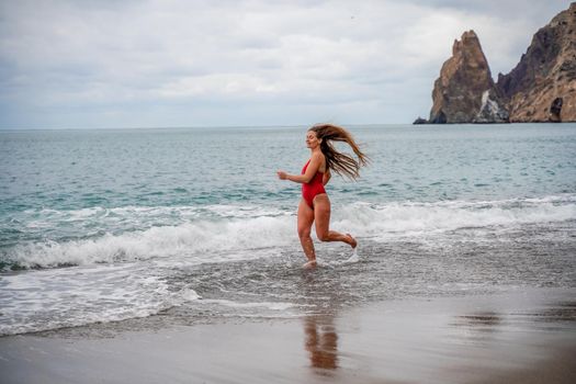 A beautiful and sexy brunette in a red swimsuit on a pebble beach, Running along the shore in the foam of the waves.