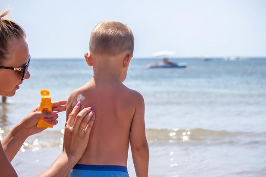 Mother puts cream on her son's back. Caring for baby skin. Sunscreens in the travel. selective focus