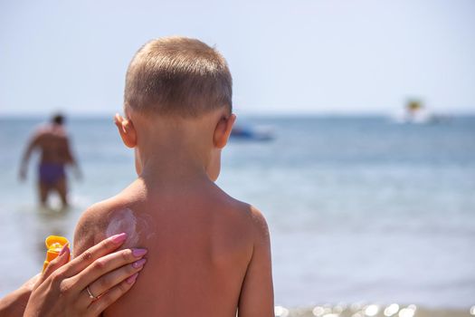 Mother puts cream on her son's back. Caring for baby skin. Sunscreens in the travel. selective focus