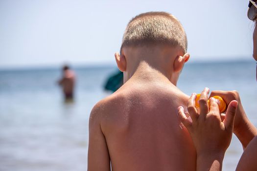 Mother puts cream on her son's back. Caring for baby skin. Sunscreens in the travel. selective focus