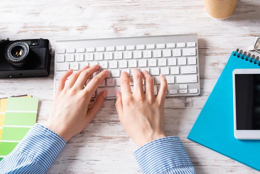 Freelancer sitting at desk and typing on wireless keyboard. Business occupation and innovation technology. Office workplace with camera and notebook. Woman blogger or columnist work at wooden desk.