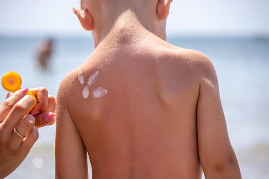 Mother puts cream on her son's back. Caring for baby skin. Sunscreens in the travel. selective focus