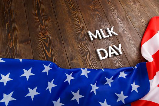 the word MLK day laid with silver metal letters on wooden surface with crumpled USA flag at lower side in diagonal perspective. MLK means Martin Luther King Jr.