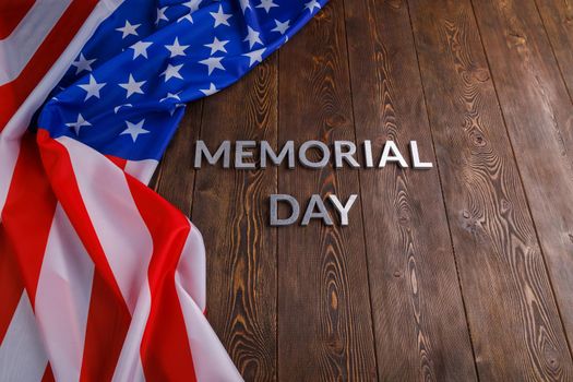 the words memorial day laid with silver metal letters on wooden board surface with crumpled usa flag.