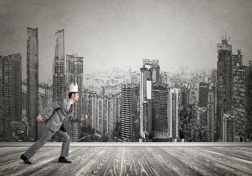 Young handsome businessman wearing white paper crown running in a hurry