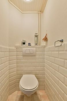 Bathroom interior with a hinged toilet surrounded by white tiles