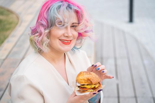 Caucasian woman with curly colored hair eating burger. Bad eating habits and love of fast food.