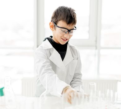 School boy wearing protection glasses doing chemistry experiment in elementary science class. Pupil with equipment tubes in lab during test