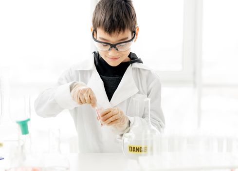 School boy wearing protection glasses doing chemistry experiment in elementary science class. Pupil with equipment tubes in lab