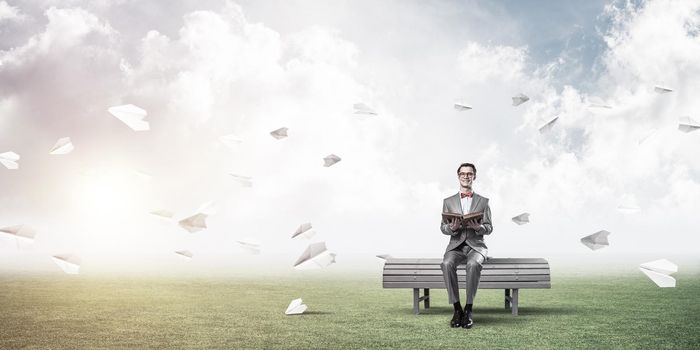 Funny man in red glasses and suit sitting on bench and reading book