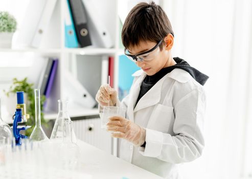 School boy wearing protection glasses doing chemistry experiment in elementary science class. Clever pupil with tubes in lab during test