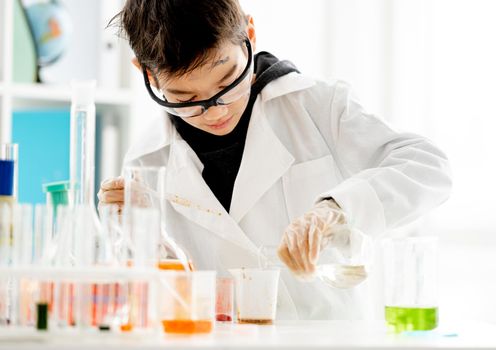 School boy wearing protection glasses with dirty face doing chemistry experiment in elementary science class. and measuring colorful liquids Clever pupil in lab