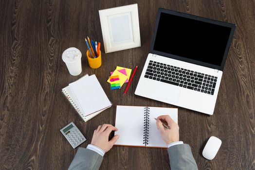 Businessman makes notes in notepad, top view workplace