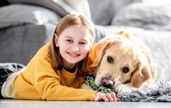 Preteen girl hugging golden retriever dog with toy lying on floor and smiling. Pretty kid child with doggy pet at home closeup portrait