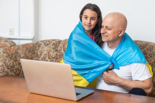 Grandfather and granddaughter with laptop and flag of Ukraine.