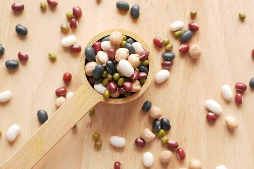 close up of mixed beans in a wooden spoon on table .