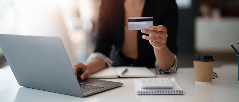 Young woman holding credit card and using laptop computer. Businesswoman working at home. Online shopping, e-commerce, internet banking, spending money, working from home concept.