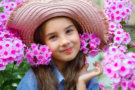 Adorable little girl in hat with pink phlox flowers, summer. Close up