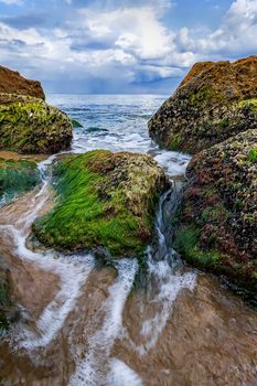 Beautiful seascape with a close view of stones with moss and flowing water between. Vertical view