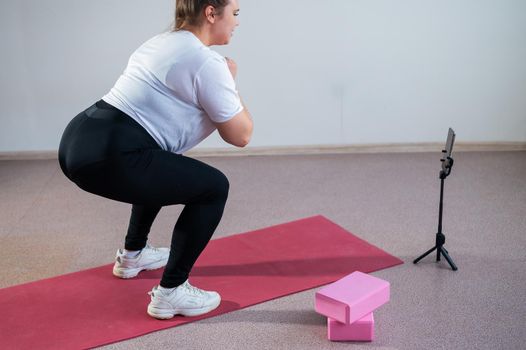 A chubby young woman is watching an online fitness lesson on a mobile phone. Distance sports training.