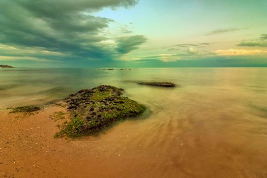 Seascape view of a calm sea with rocks with moss. Beauty sky with clouds at the horizon. 