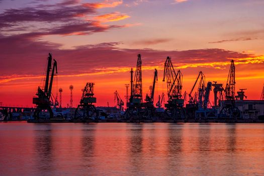 Silhouettes of port cranes at stunning red sunset. Cargo ship terminal at the twilight scene.