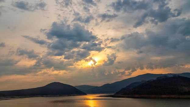 Stunning view of a lake among hills and mountains with sun reflection