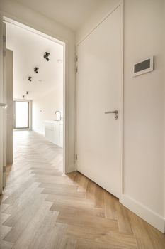 A narrow corridor with parquet floor leading inside a cozy house in white