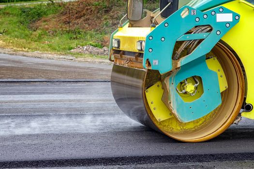 Close view of drum roller at the construction site, working on the new road with smoke