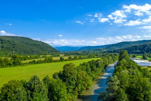 Aerial view from drone of the vast green landscape with river, hills and blue sky