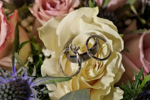 High Angle Close up f White Gold and Diamond Wedding and Engagement Rings on White and Pink Rose Bouquet