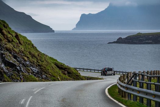 Cloudy day with road near fjord and car in Faroe Islands