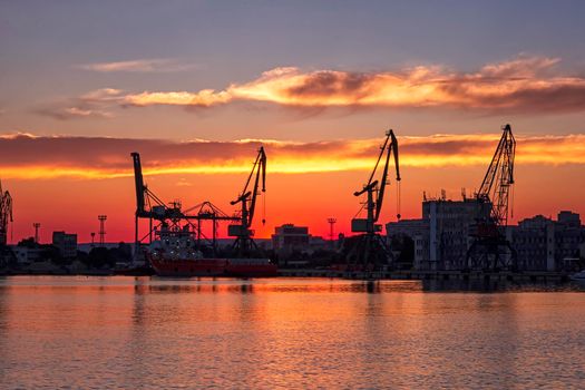 Silhouettes of port cranes at stunning red sunset. Cargo ship terminal at the twilight scene.